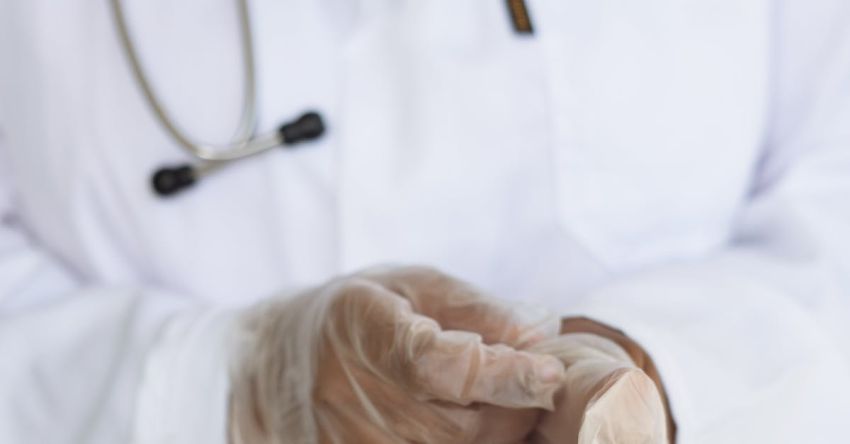 Crop Diseases - Faceless ethnic medical worker in lab coat and stethoscope taking of transparent gloves after approaching patients for examination in modern hospital